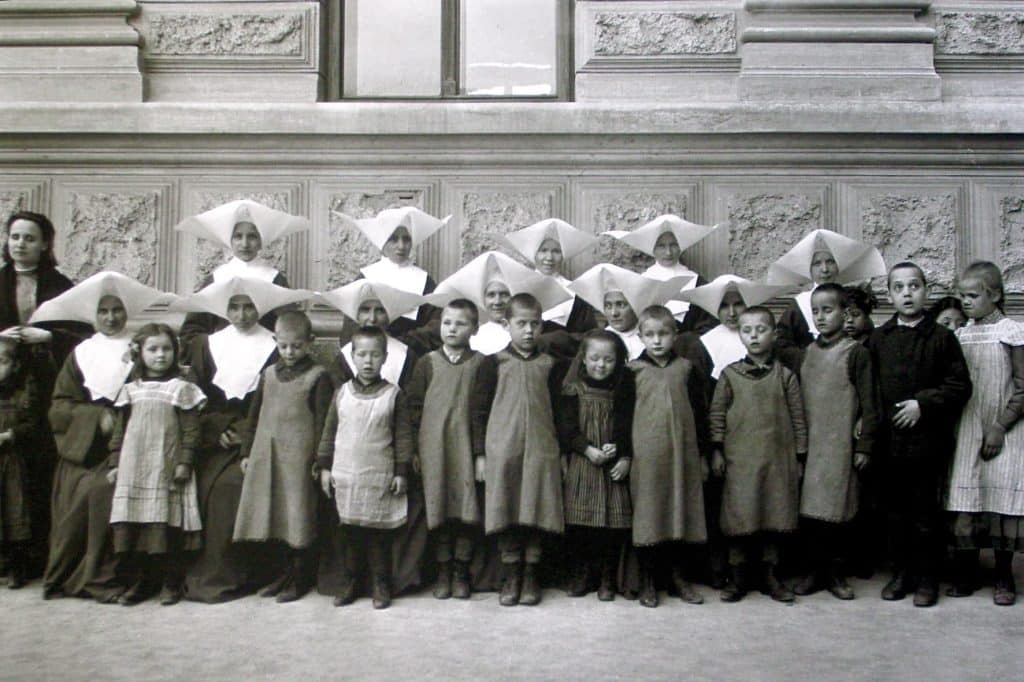 Altes Schwarz-Weiß-Foto von einer Gruppe Kindern und Ordensschwestern vor einem historischen Gebäude.