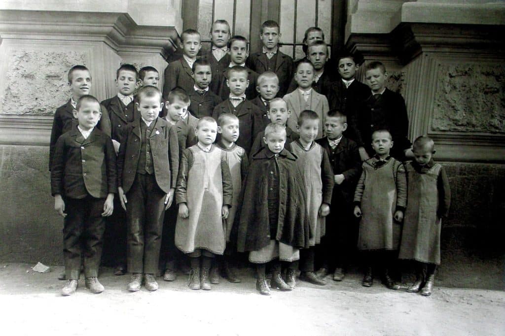 Altes Schwarz-Weiß-Foto von einer Gruppe Buben vor einem historischen Gebäude.